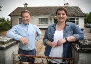 Cheap Irish Homes Presenters Kieran Mc Carthy and Maggie Molloy leaning on gate wall with old bungalow in background landscape